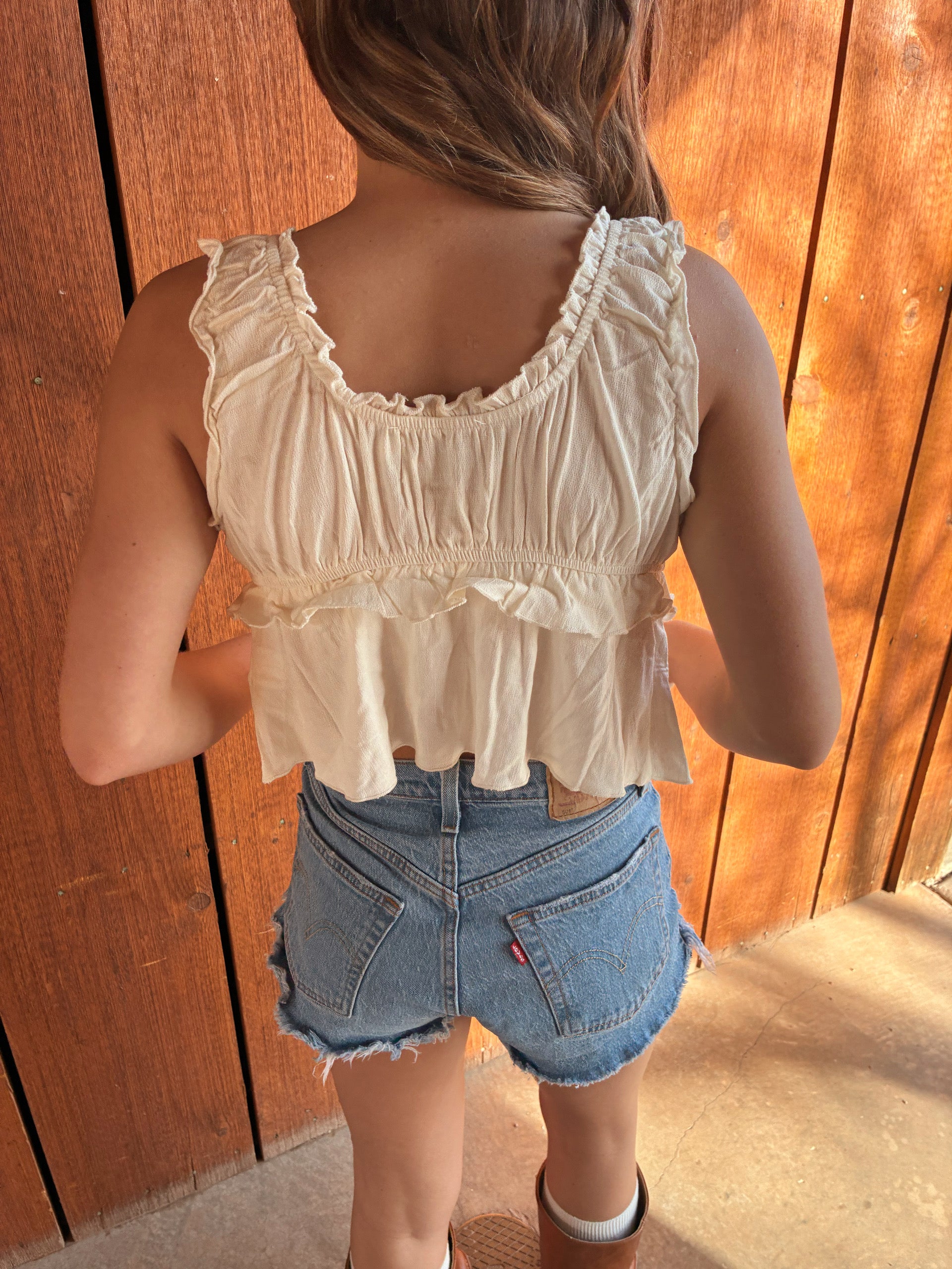 Cream ruffle tie front tank top from Nectar Clothing styled with denim shorts and brown western boots for a summer cowgirl outfit at VNTGcowgirl western boutique.