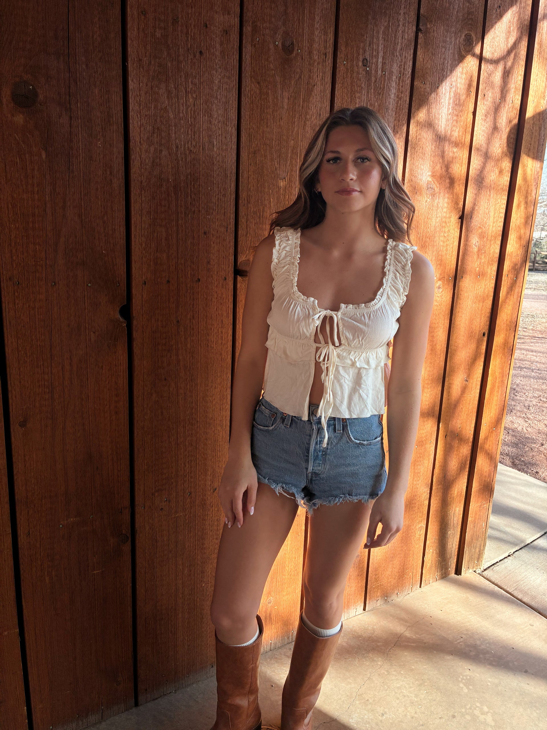 Cream ruffle tie front tank top from Nectar Clothing styled with denim shorts and brown western boots for a summer cowgirl outfit at VNTGcowgirl western boutique.